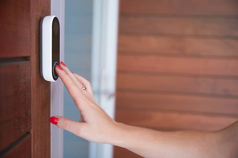 Woman pressing the camera doorbell button .