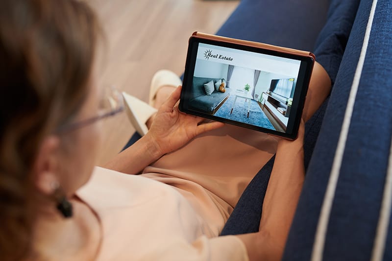Woman on a couch searching for rental properties on her tablet.