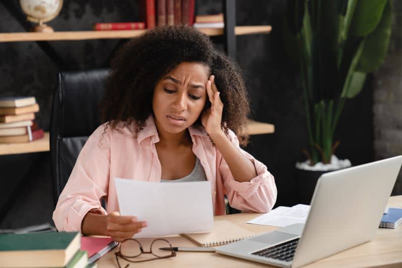 Woman with a migraine going over real estate financial options sitting at her desk with a laptop open.