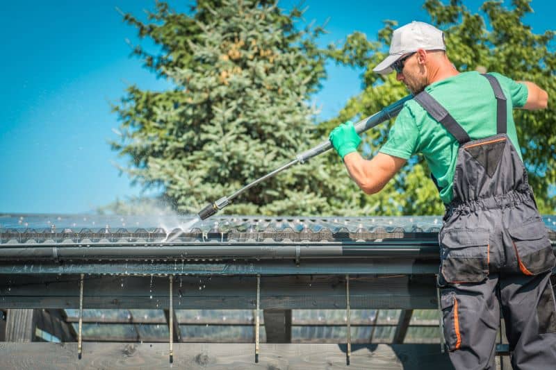 A man cleaning out a gutter with a power wash machine.