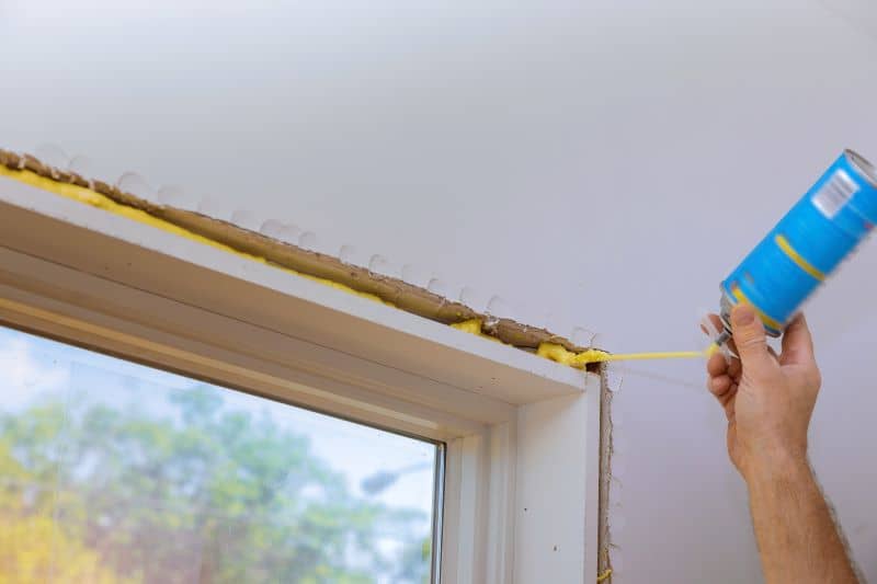 A man using a spray foam to insulate the window of a home.